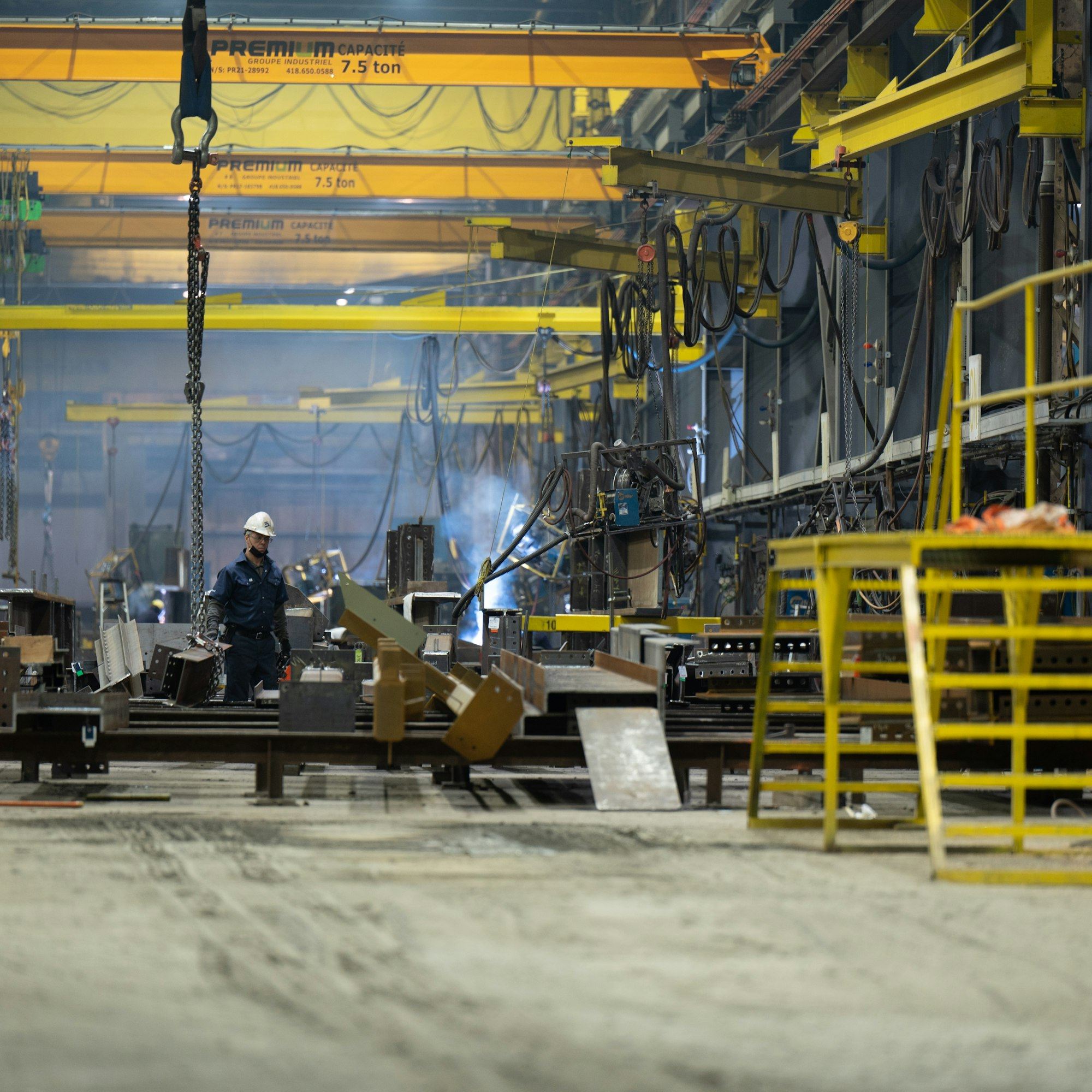 Fabrication workshop interior with overhead crane and a welder at work